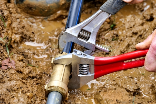 Plumber shutting off water supply and inspecting burst pipe in a flooded residential basement