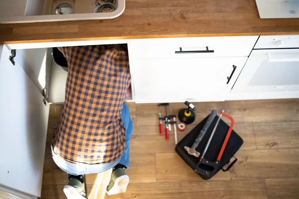 Poly-B Plumbing technician checking under-sink plumbing during a scheduled maintenance visit in North Bay